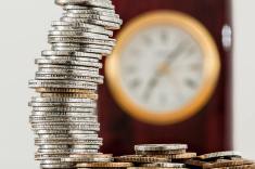 Piles of coins with a clock in the background.