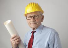 Older man in a hard hat carrying some drawings.