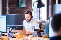 Man at a computer with a head set on.