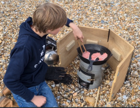 Boy cooking bacon outdoors.