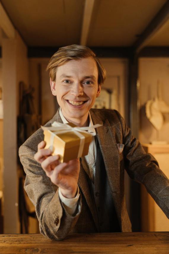 A salesman in a suite with a big smile and a gift in his hand.