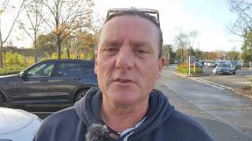 Man talking at a camera walking along in a car park.