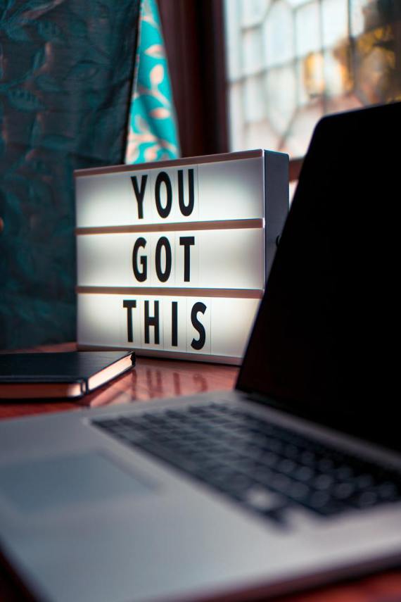 An illuminated sign with "You Got this" written on it besides a laptop and note book.